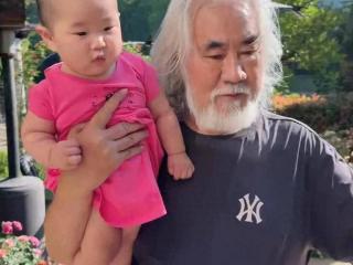 张纪中抱孩子浇花，院子里有花有树绿化非常好，媲美公园